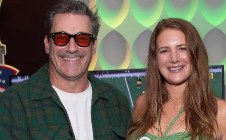 Jon Hamm, 55, and pregnant wife Anna Osceola, 38, pose with a New York Jets baby onesie as they head to Green Bay Packers game